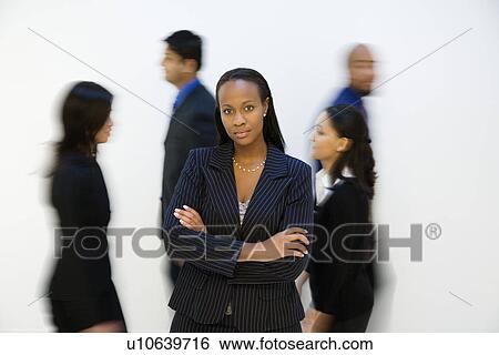 African-American businesswoman standing with arms crossed while others walk by. View Large Photo Image Stock Photograph - African-American businesswoman standing with arms crossed while others walk by.. Fotosearch