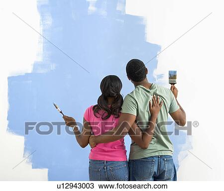 Stock Image - African American couple standing together looking at half-painted wall.. Fotosearch