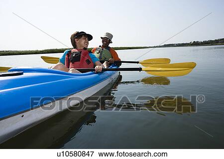 Stock Photo - African American middle-aged couple sitting in kayak on lake smiling and laughing.. Fotosearch