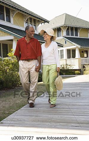 Stock Photo - African American middle aged couple holding hands strolling on wooden walkway.. Fotosearch