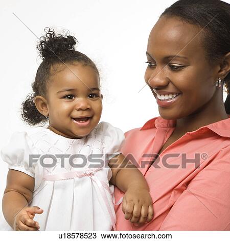 Stock Image - African American woman holding infant girl standing against white background.. Fotosearch