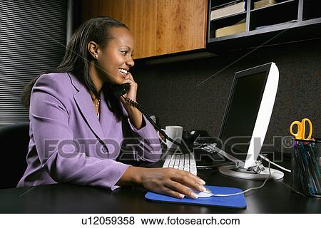 African-American young adult smiling business woman talking on phone and working at computer in office. View Large Photo Image Stock Photo - African-American young adult smiling business woman talking on phone and working at computer in office.. Fotosearch