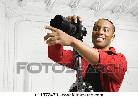 Stock Photo - African American young male adult with camera and pointing.. Fotosearch