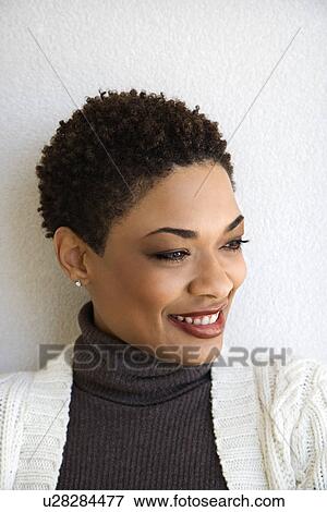 Stock Photo - Close up head and shoulder of African-American woman standing against white wall smiling with head turned to side.. Fotosearch