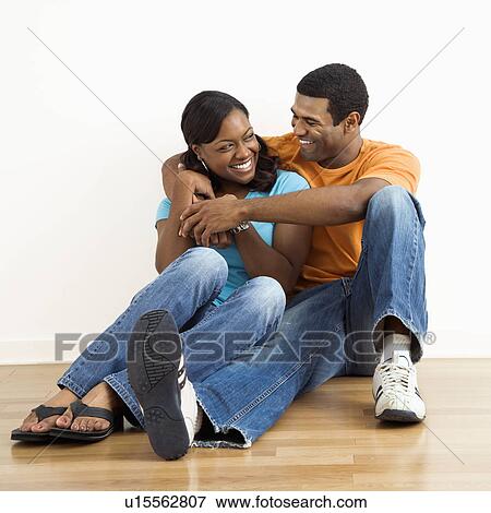 Stock Photo - Happy couple sitting on floor snuggling. Fotosearch