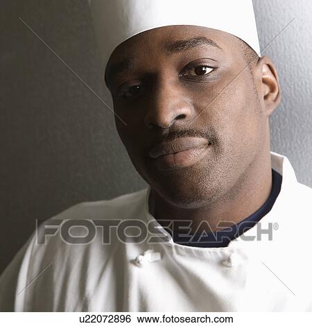 Stock Photograph - Head shot of African-American male chef wearing traditional uniform and toque looking at viewer.. Fotosearch