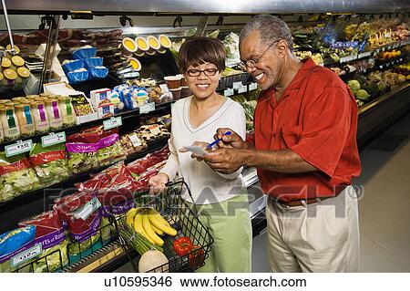 Stock Photograph - Man and woman in grocery store smiling and pointing at shopping list. Fotosearch