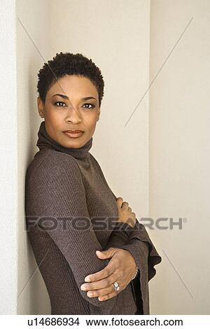 Picture - photograph, image, color, vertical, person, woman, female, short hair, looking at viewer, arms crossed, leaning, against wall, standing, indoors, young woman, portrait, 060309e0014, 30-35 years, eye contact, half-length, one person only, African-American, mid-adult woman. Fotosearch