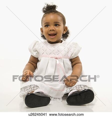 Stock Image - Portrait of African American infant girl sitting against white background.. Fotosearch