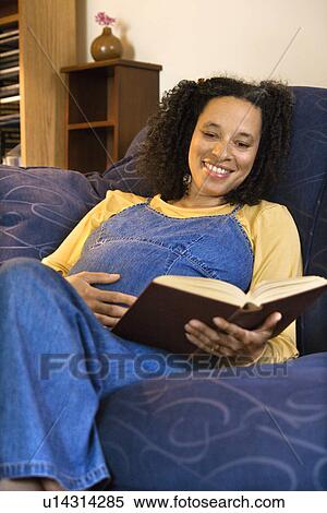 Stock Photography - Portrait of pregnant female reading a book and holding her stomach.. Fotosearch