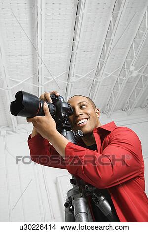 Picture - Young male looking through camera on tripod. Fotosearch