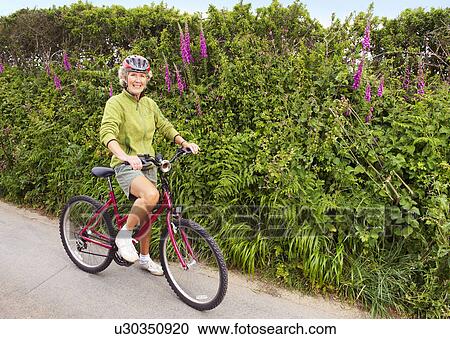 Stock Image - Senior woman posing with bicycle. Fotosearch