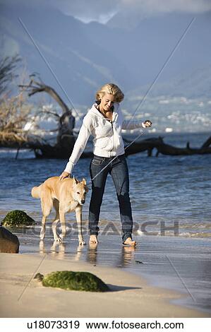 Stock Photo - Caucasian woman walking brown dog on leash on Maui, Hawaii beach.. Fotosearch