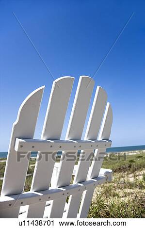 Stock Image - Empty white adirondack chair facing beach. Fotosearch