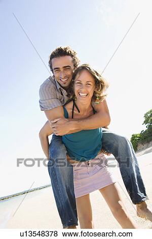 Mid-adult Caucasian woman giving man piggyback ride on beach. View Large Photo Image Stock Photo - Mid-adult Caucasian woman giving man piggyback ride on beach. . Fotosearch