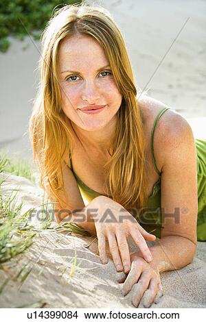 Portrait of pretty redheaded woman lying in sand looking at viewer. View Large Photo Image Picture - Portrait of pretty redheaded woman lying in sand looking at viewer.. Fotosearch