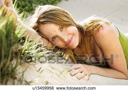 Stock Photo - Portrait of pretty redheaded woman lying in sand looking at viewer.. Fotosearch
