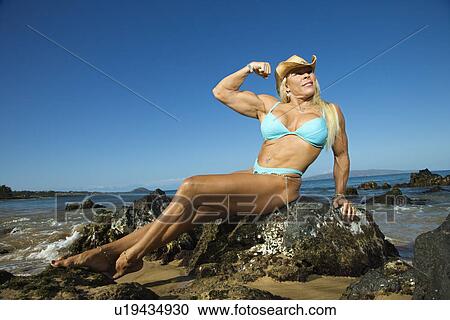 Pretty Caucasian mid adult woman bodybuilder in bikini sitting on rock flexing bicep on beach. View Large Photo Image Stock Image - Pretty Caucasian mid adult woman bodybuilder in bikini sitting on rock flexing bicep on beach.. Fotosearch