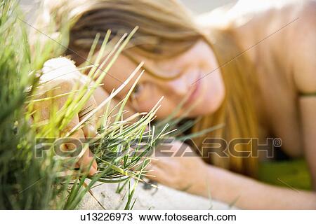 Stock Image - Selective focus portrait of young redheaded woman lying in grass looking at viewer.. Fotosearch