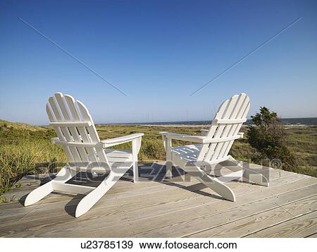 Stock Photo - Two adirondack chairs on wooden deck overlooking beach at Bald Head Island, North Carolina.. Fotosearch