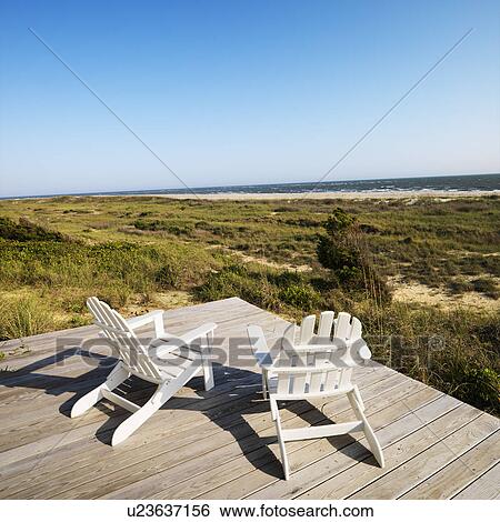 Two adirondack chairs on wooden deck overlooking beach at Bald Head Island, North Carolina. View Large Photo Image Stock Photograph - Two adirondack chairs on wooden deck overlooking beach at Bald Head Island, North Carolina.. Fotosearch