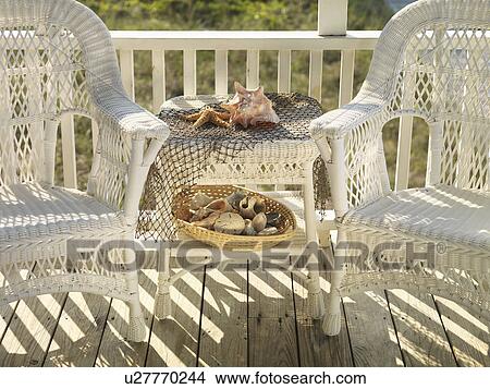 Picture - Two wicker chairs with table between them with seashells.. Fotosearch
