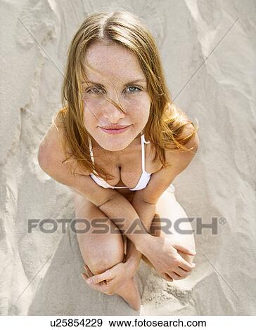 Stock Photo - Woman sitting on beach wearing bikini . Fotosearch