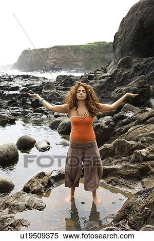Young adult female standing on rocky shore with arms outstretched and eyes closed. View Large Photo Image Stock Photography - Young adult female standing on rocky shore with arms outstretched and eyes closed.. Fotosearch