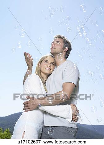 Stock Photo - Couple in sun catching bubbles. Fotosearch