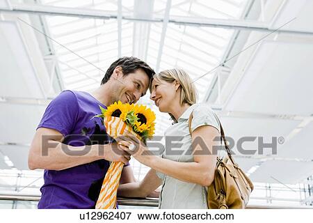Stock Photo - Couple smiling exchanging flowers. Fotosearch