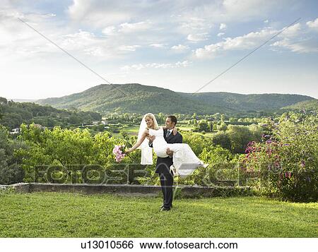 Stock Photograph - Groom carrying bride in garden. Fotosearch