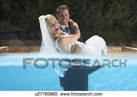 Stock Photography - Groom carrying bride in pool. Fotosearch