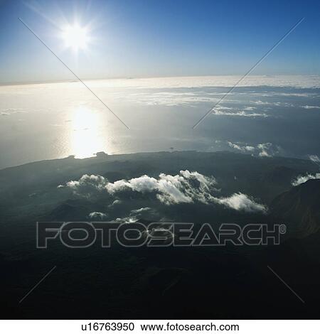 Aerial view of mountainous terrain in Maui, Hawaii with sun shining off the Pacific ocean in background. View Large Photo Image Stock Image - Aerial view of mountainous terrain in Maui, Hawaii with sun shining off the Pacific ocean in background.. Fotosearch
