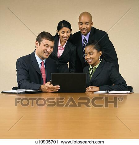 Stock Image - Businesspeople gathered around laptop computer looking at monitor and smiling.. Fotosearch