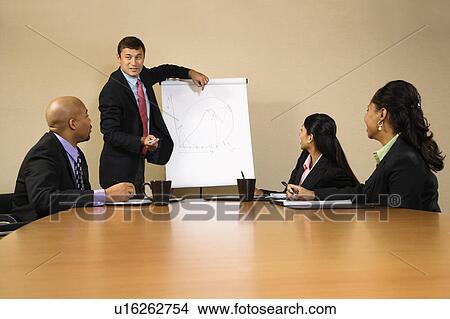 Picture - Businesspeople sitting at conference table while businessman gives presentation. Fotosearch