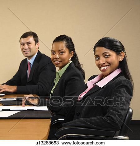 Stock Image - Businesspeople sitting at conference table smiling. Fotosearch