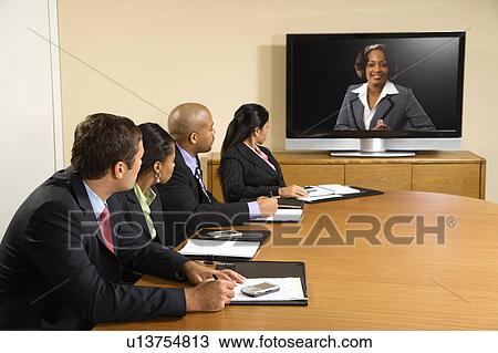 Stock Image - Businesspeople sitting at conference table looking at flat screen display. Fotosearch