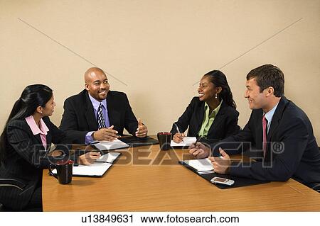 Stock Image - Businesspeople sitting at conference table smiling. Fotosearch