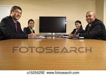 Businesspeople sitting at conference table smiling with flat screen tv View Large Photo Image Stock Image - Businesspeople sitting at conference table smiling with flat screen tv. Fotosearch