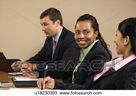 Stock Image - Businesspeople sitting at conference table talking and smiling.. Fotosearch