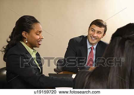 Stock Image - Businesspeople sitting at conference table talking and smiling. Fotosearch