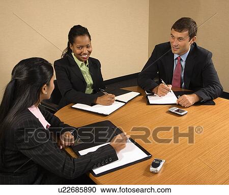 Stock Image - Businesspeople sitting at conference table talking and smiling.. Fotosearch