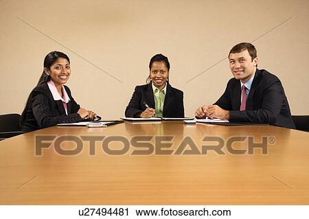 Stock Image - Businesspeople sitting at conference table smiling.. Fotosearch