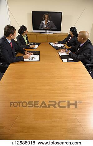 Stock Photo - Businesspeople sitting at conference table looking at flat screen display. Fotosearch