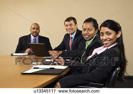 Stock Photo - Businesspeople sitting at conference table smiling.. Fotosearch