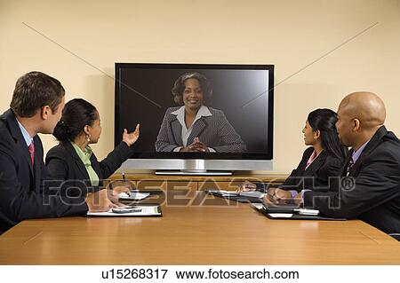 Stock Photo - Businesspeople sitting at conference table looking at flat screen display.. Fotosearch