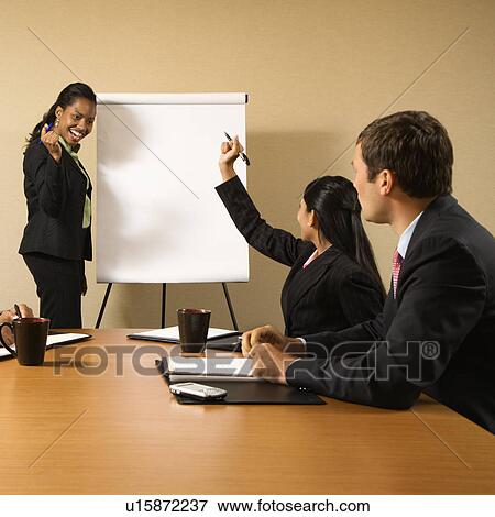 Stock Photo - Businesspeople sitting at conference table while businesswoman gives presentation.. Fotosearch