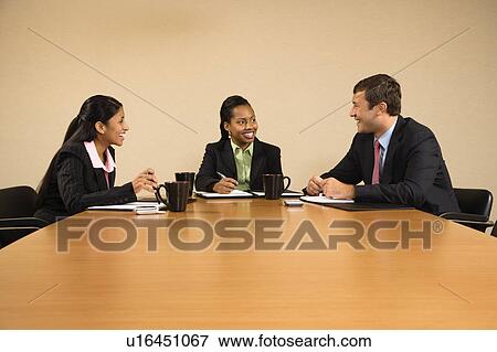 Stock Photo - Businesspeople sitting at conference table talking and smiling.. Fotosearch