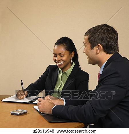 Stock Photo - Businesspeople sitting at conference table talking and smiling.. Fotosearch