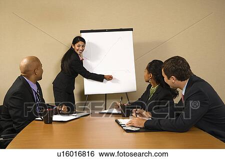 Stock Photograph - Businesspeople sitting at conference table smiling while businesswoman gives presentation.. Fotosearch